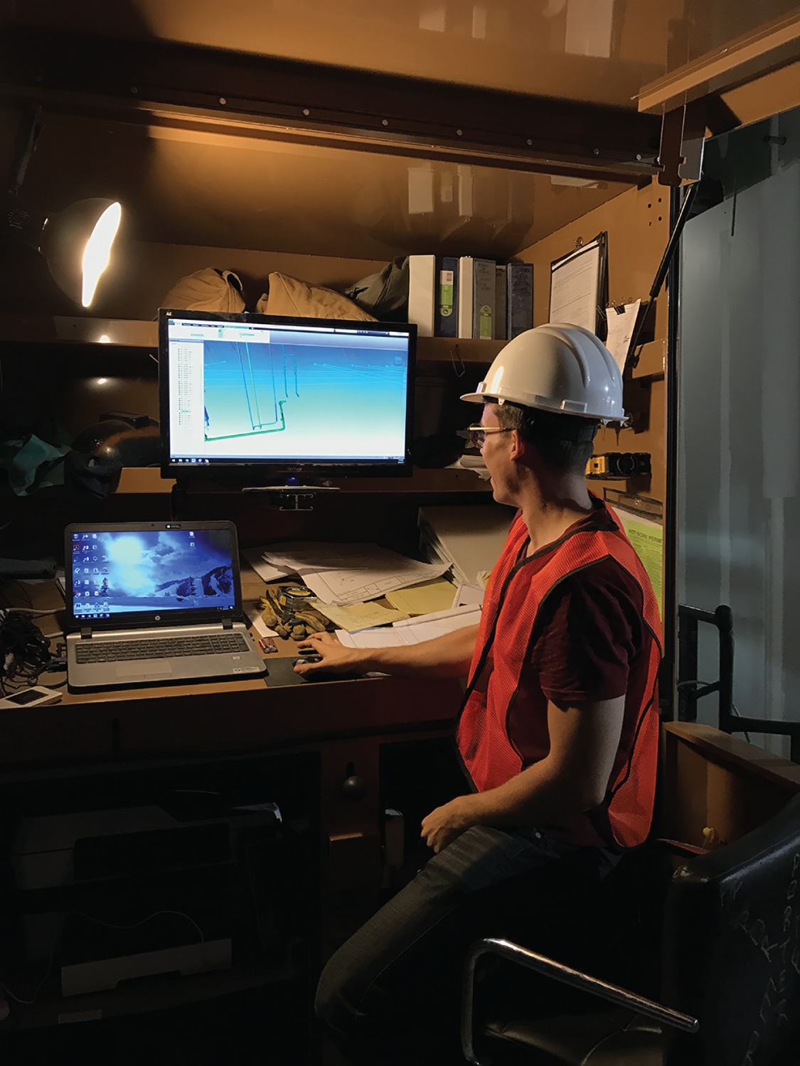 Photograph depicting a worker in front of a laptop and desktop computer in a subcontractor BIM station near the work face.