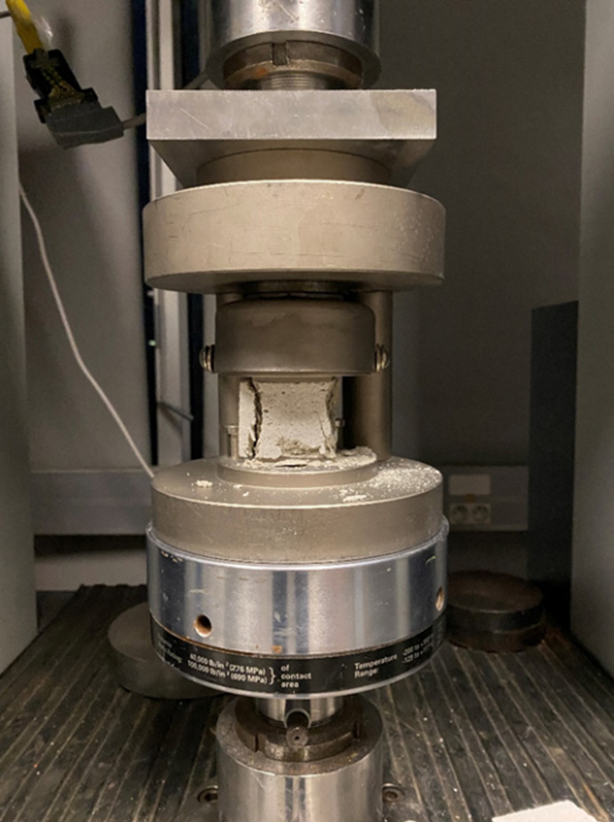 An image features a machine equipped with a long tube, likely utilized for conducting a compression test on cubic specimens for mortar on a specified scale. This device may be categorized as an indoor appliance, potentially linked to kitchen or home use.